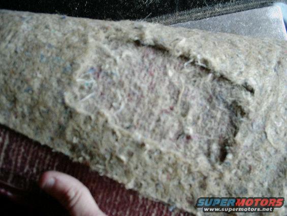 Damaged carpet padding with visible fibers and some colored flecks