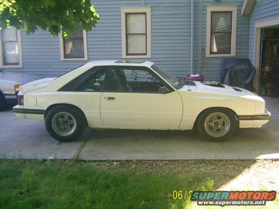 White coupe with aftermarket wheels parked in driveway, hood scoop visible