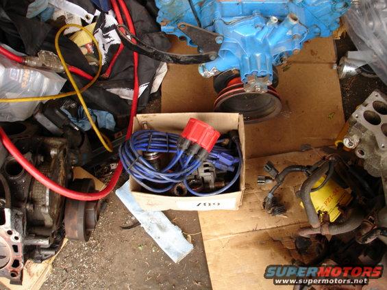 Engine parts including a blue engine block, distributor cap, spark plug wires, and hoses on cardboard