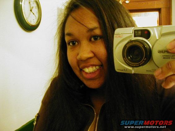 Woman taking a selfie with a silver digital camera, clock on wall