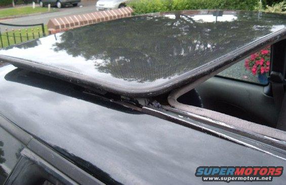 Close-up of a car's sunroof, showing the seal and the reflective surface. Other cars are visible in the background