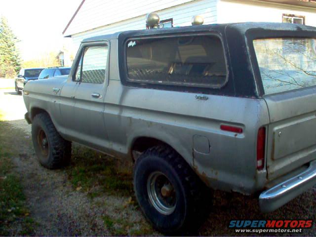Side view of a silver Ford Bronco with a black top. It has two lights on the roof
