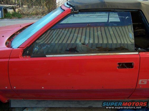 Red convertible sports car side view, door handle missing, top is up