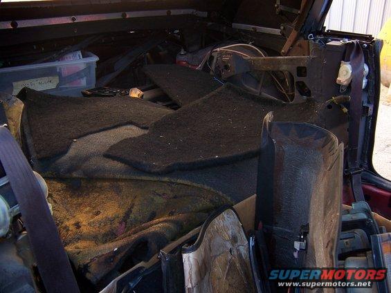 Interior of a car with disassembled carpeting and parts. Readable text on a plastic bin