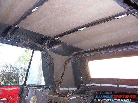 Interior view of car's roof structure and window frame, showing exposed metal and fabric