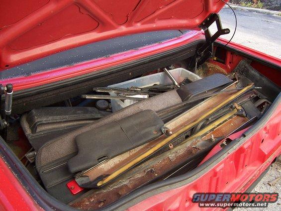 red car trunk packed with various car parts, including trim pieces and what looks like sun visors