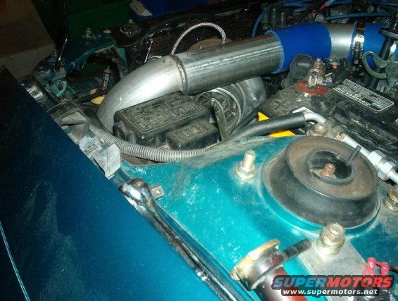 Engine bay showing turbo piping, fuse box, and battery terminal