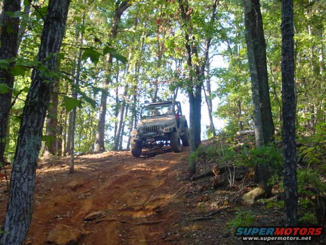 2004 Jeep TJ driving up a dirt hill in a wooded area