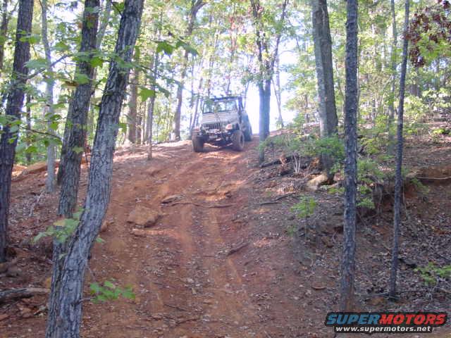 Jeep Wrangler climbing a steep, wooded dirt trail. It's a 2004 Jeep TJ