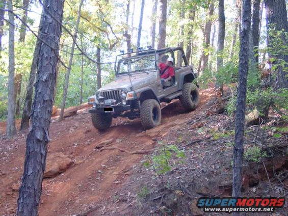 2004 Jeep TJ driving up a steep dirt trail in a wooded area