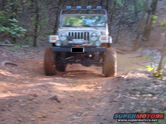 Silver Jeep Wrangler on a dirt trail, front view. Modified with large tires and winch