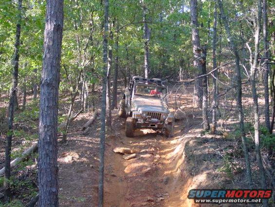 Silver 2004 Jeep TJ climbing a steep, rutted dirt trail in a wooded area