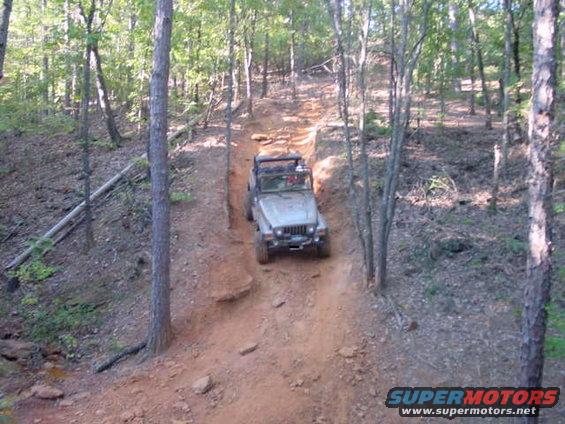 Silver Jeep Wrangler climbing a steep dirt trail in a wooded area