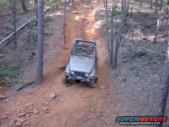 Silver 2004 Jeep TJ climbing a steep, narrow dirt trail in a wooded area