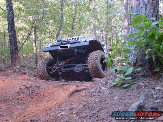 Jeep Wrangler on a dirt trail, front view. Large tires, lifted suspension, dark grille
