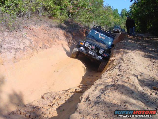 Black 2004 Jeep TJ navigating a steep dirt ditch off-road, another Jeep visible in background
