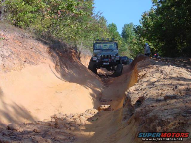 Jeep TJ driving down a sandy off-road trail with trees on either side