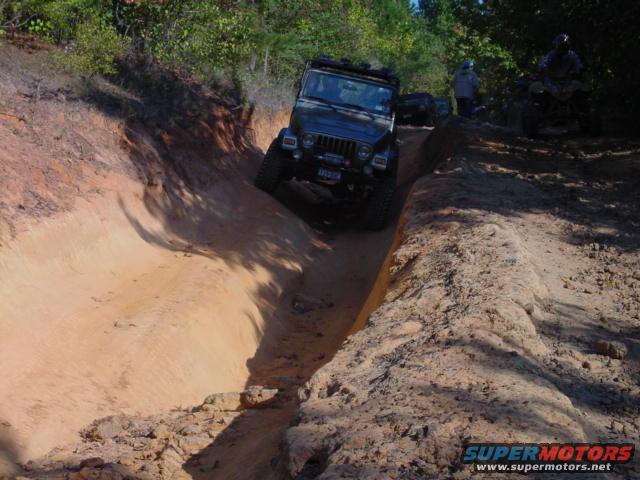 Black Jeep TJ driving down a sandy ditch, front-left wheel angled up