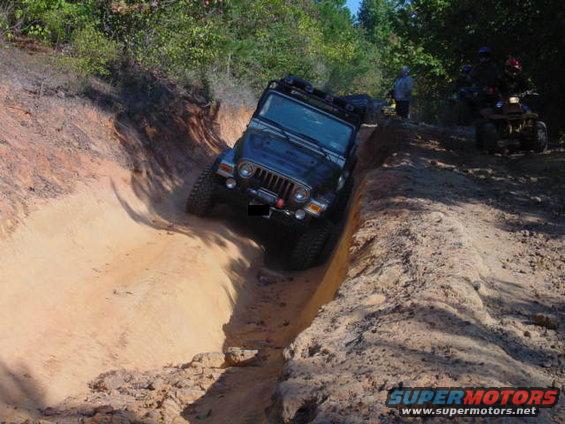 Black Jeep Wrangler TJ on a dirt trail, with an ATV in the background