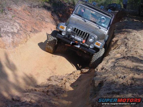 Silver Jeep TJ navigating a steep dirt incline, another vehicle visible in the background
