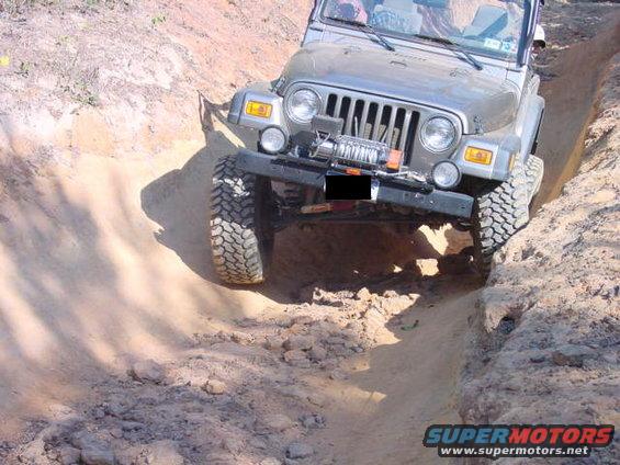 Jeep TJ going down a dirt trench, front view. It has a winch on the bumper