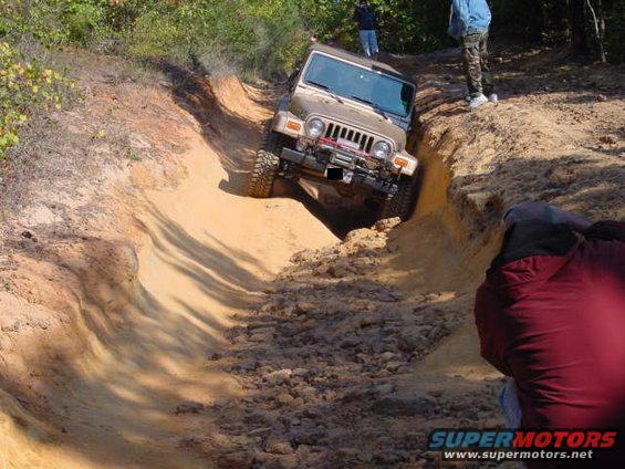 2004 Jeep TJ navigating a steep dirt rut on an off-road trail