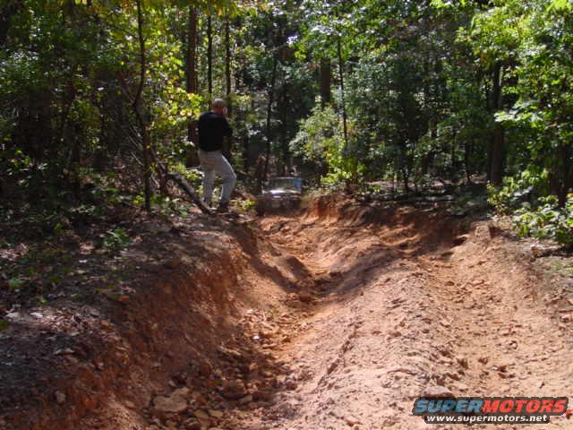 Person standing on dirt path next to off-road vehicle in wooded area