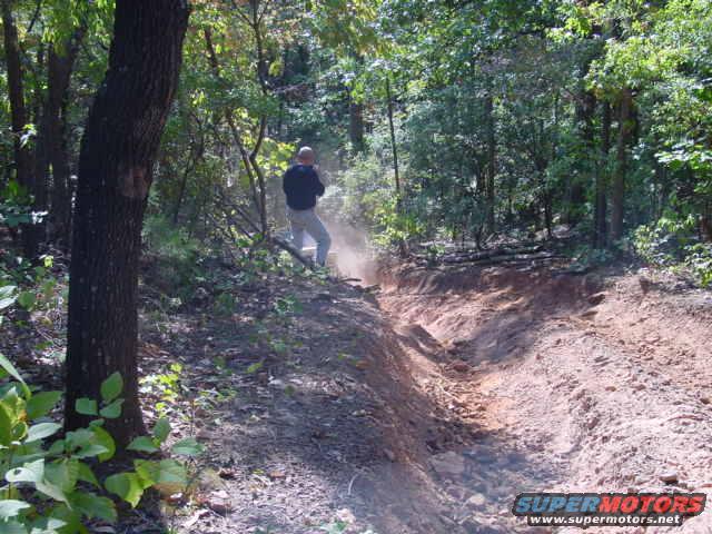 Dirt trail in woods with a person standing on the side, kicking up dust
