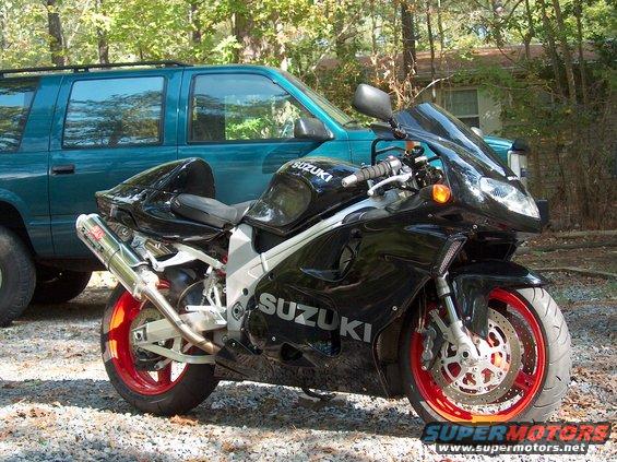 Black Suzuki sportbike parked in front of a teal SUV. Red rims on the bike