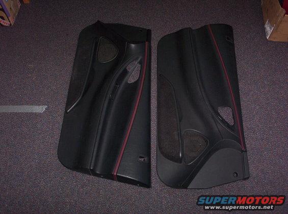 Two black car door panels with red trim and speaker grilles on a carpeted floor