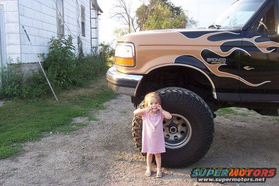 1995 Ford Bronco with flame decals and a young child standing next to the front tire