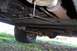 1985 Jeep Grand Wagoneer - The underside of a vehicle shows its frame, exhaust, and suspension components with a tire visible.