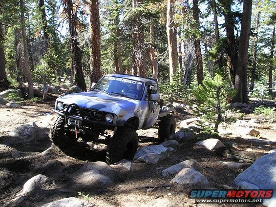 Off-road truck with large tires and custom bumper driving on a rocky trail