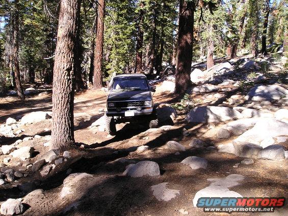 Black SUV with a lifted suspension on a rocky, wooded trail