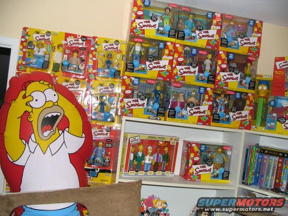 Collection of The Simpsons action figures and merchandise, including a Homer Simpson pillow