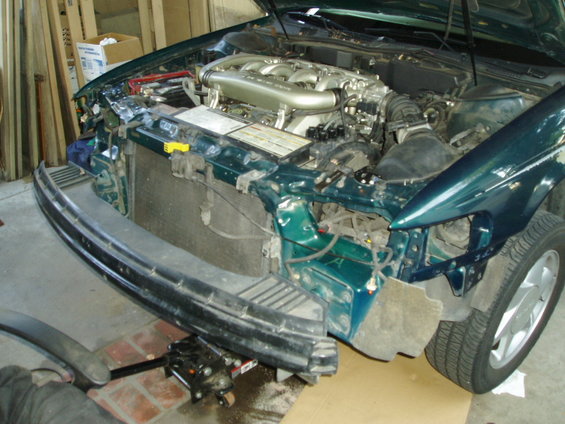 Green car engine and front end with bumper removed, jack under car
