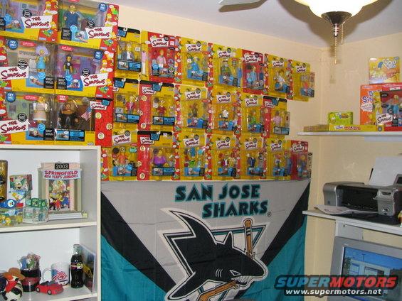 Wall covered in The Simpsons action figures, San Jose Sharks flag, and shelves with toys and a printer