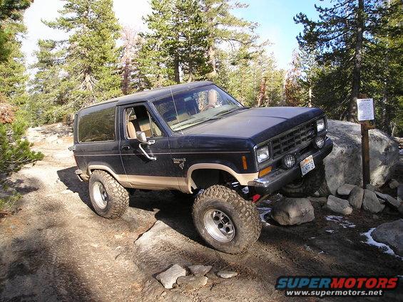 1986 Ford Bronco II on rocky trail, front passenger side visible, trees and sky in background