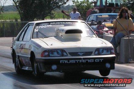 White Ford Mustang GT drag car with hood scoop, front wheels off the ground