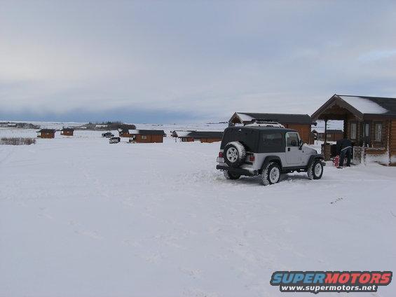 Silver 2001 Jeep TJ parked in snow near cabins, with another vehicle in the distance