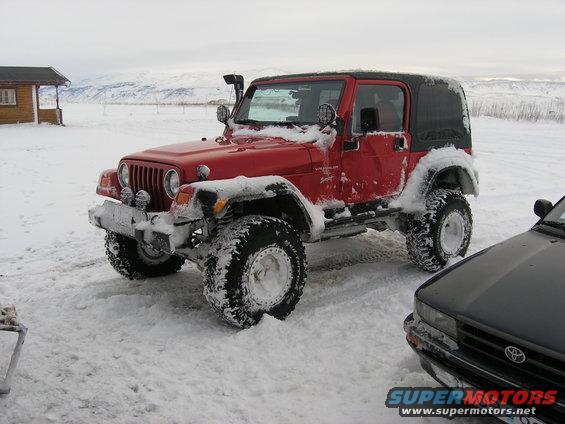 Red 2001 Jeep TJ with snorkel and aftermarket wheels parked in snow next to a black car