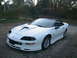 1996 Chevrolet Camaro - A white 1996 Chevrolet Camaro is parked on a gravel surface with trees and foliage behind it.