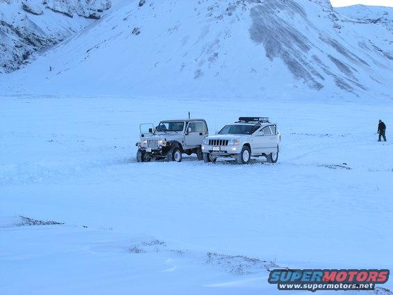 Two SUVs parked in a snowy field with mountains in the background