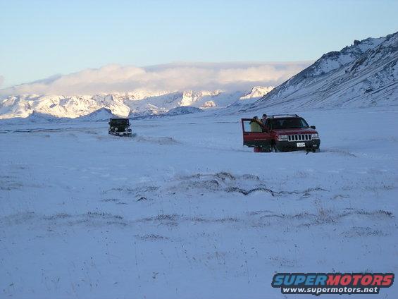 Two SUVs parked in a vast snowy field with mountains in the background