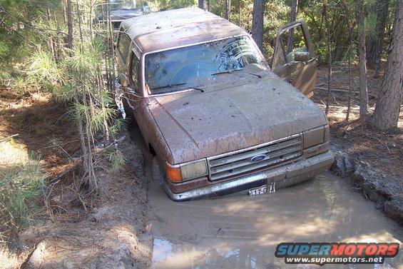 Mud-covered 1987 Ford Bronco stuck in a muddy ditch, front 3/4 view