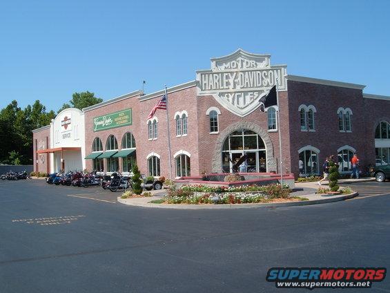 Harley-Davidson dealership building exterior with motorcycles parked in front and a green car on the right