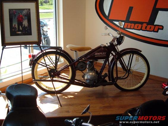 Simplex Automatic motorcycle with a tan seat and spoked wheels, displayed indoors