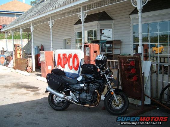 2001 Suzuki Bandit motorcycle parked next to an APCO gas sign and vintage gas pumps