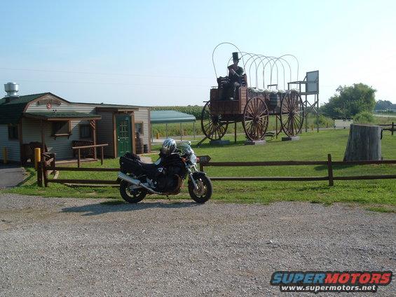 Motorcycle parked by a building with a covered wagon display