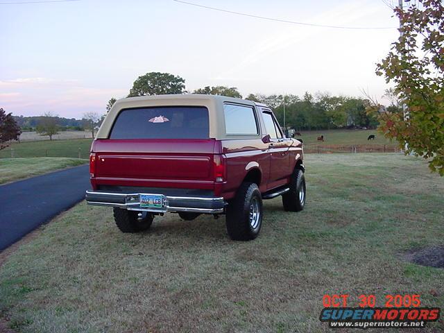 Maroon Ford Bronco with tan top, lifted suspension, seen from rear